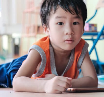 Young Asian child laying on the floor playing with a smartphone.