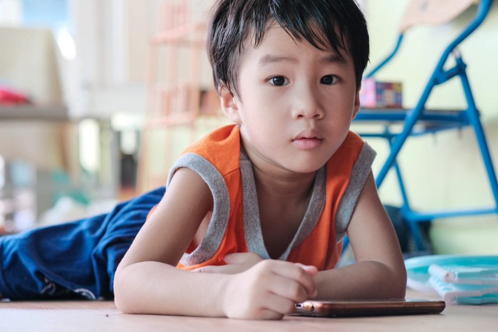 Young Asian child laying on the floor playing with a smartphone.