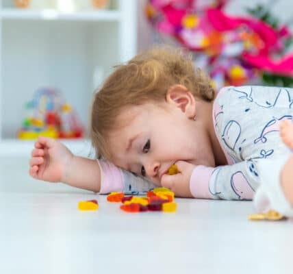 Baby laying on the floor eating gummy bears.