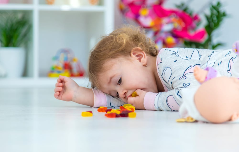 Baby laying on the floor eating gummy bears.