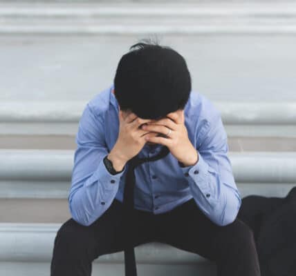 Photo of a man sitting on the steps of a building with his head in his hands in a sign of anguish.