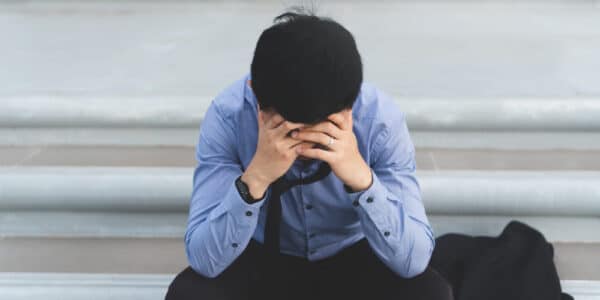 Photo of a man sitting on the steps of a building with his head in his hands in a sign of anguish.
