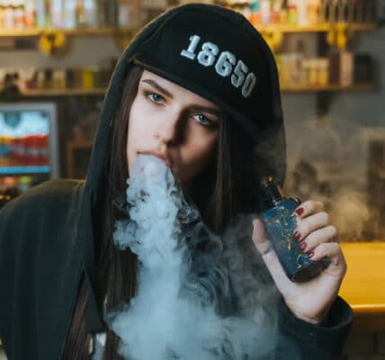 Close-up photo of a young woman in a cap smoking an electronic cigarette at the vape shop.