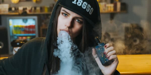 Close-up photo of a young woman in a cap smoking an electronic cigarette at the vape shop.
