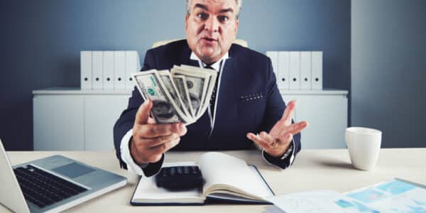 Photo of a healthcare industry executive at a desk in his office with a computer open and a hand full of one hundred dollar bills.