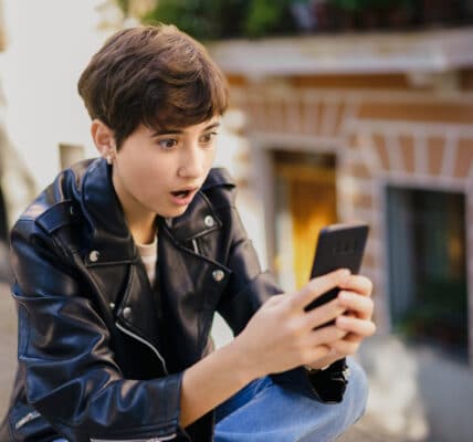 Photo of a teenager in a leather jacket who sees something shocking on their phone.