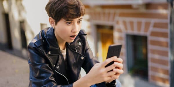 Photo of a teenager in a leather jacket who sees something shocking on their phone.