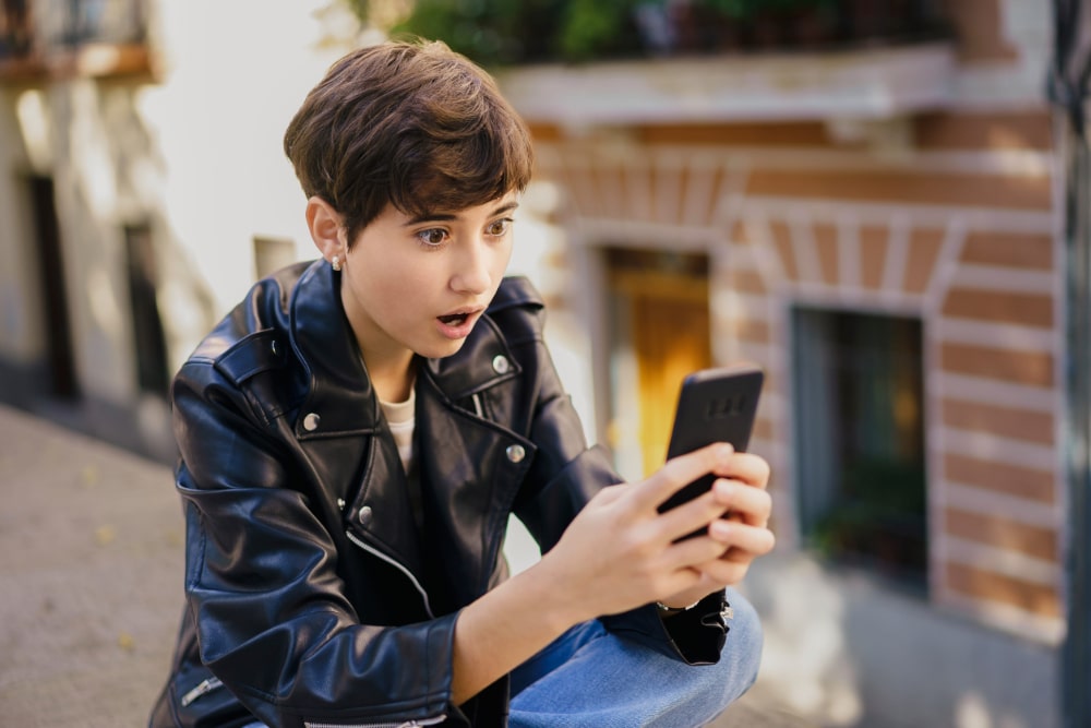 Photo of a teenager in a leather jacket who sees something shocking on their phone.