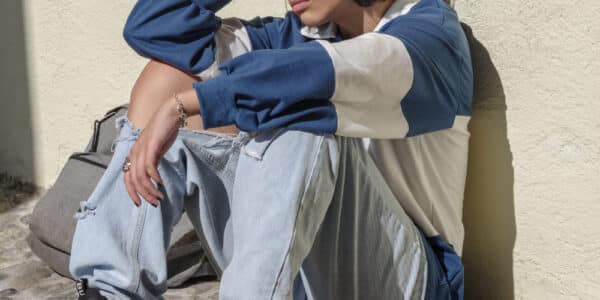 Photo of Latin teenager sitting on the ground who looks sad and distressed.
