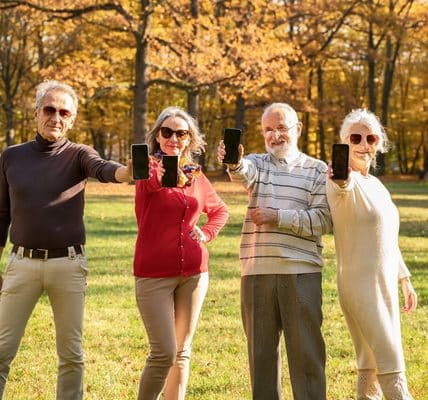 Four seniors outdoors are showing their phones.