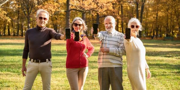 Four seniors outdoors are showing their phones.