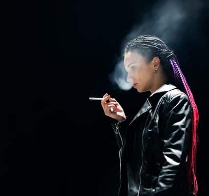A lone figure of a young woman shown smoking.
