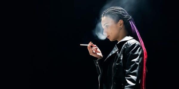 A lone figure of a young woman shown smoking.