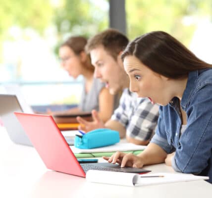 Photo of three colleges students discovering shocking news on their notebook computers at the same time.