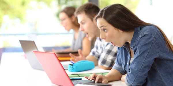 Photo of three colleges students discovering shocking news on their notebook computers at the same time.