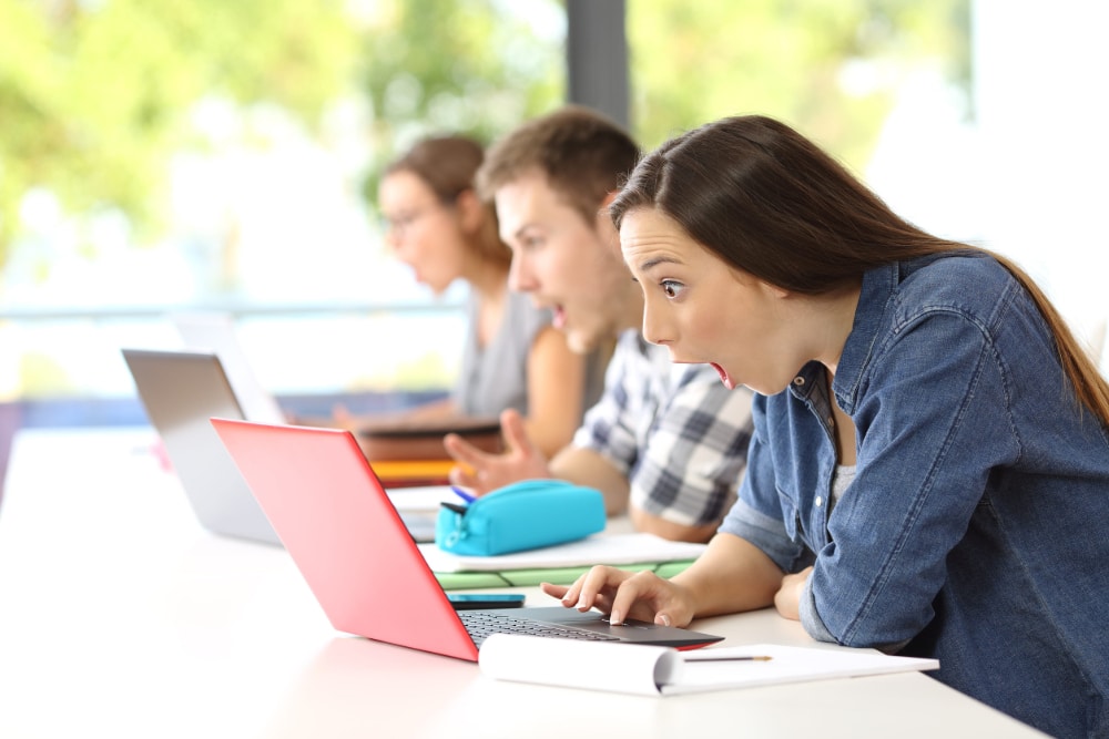 Photo of three colleges students discovering shocking news on their notebook computers at the same time.