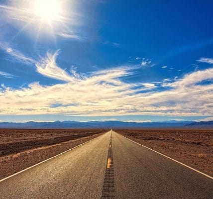 An image with a vast landscape that includes a wide road and blue sky.