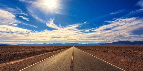 An image with a vast landscape that includes a wide road and blue sky.